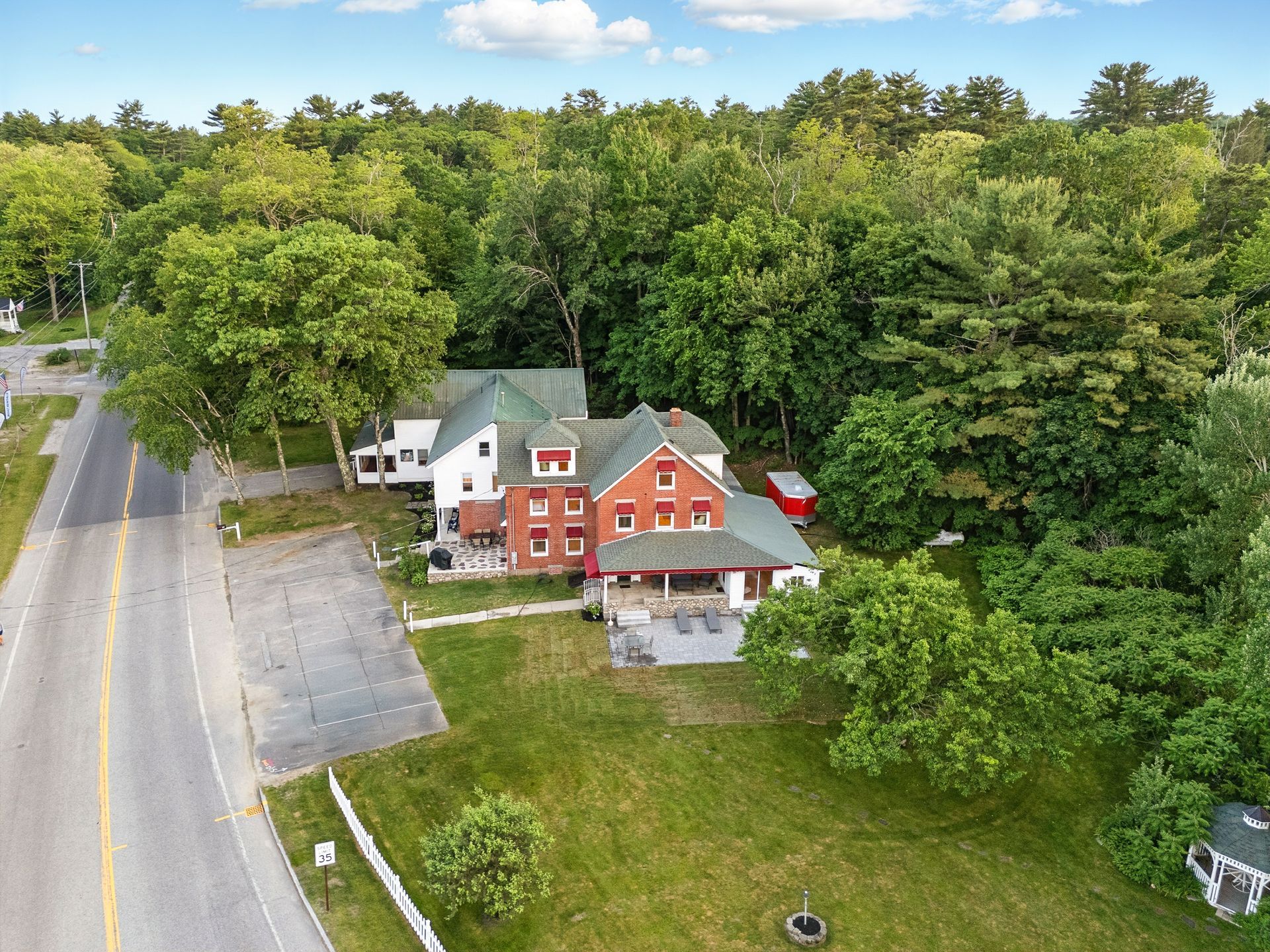 Aerial view of a brick house with a green roof, surrounded by trees and a road.