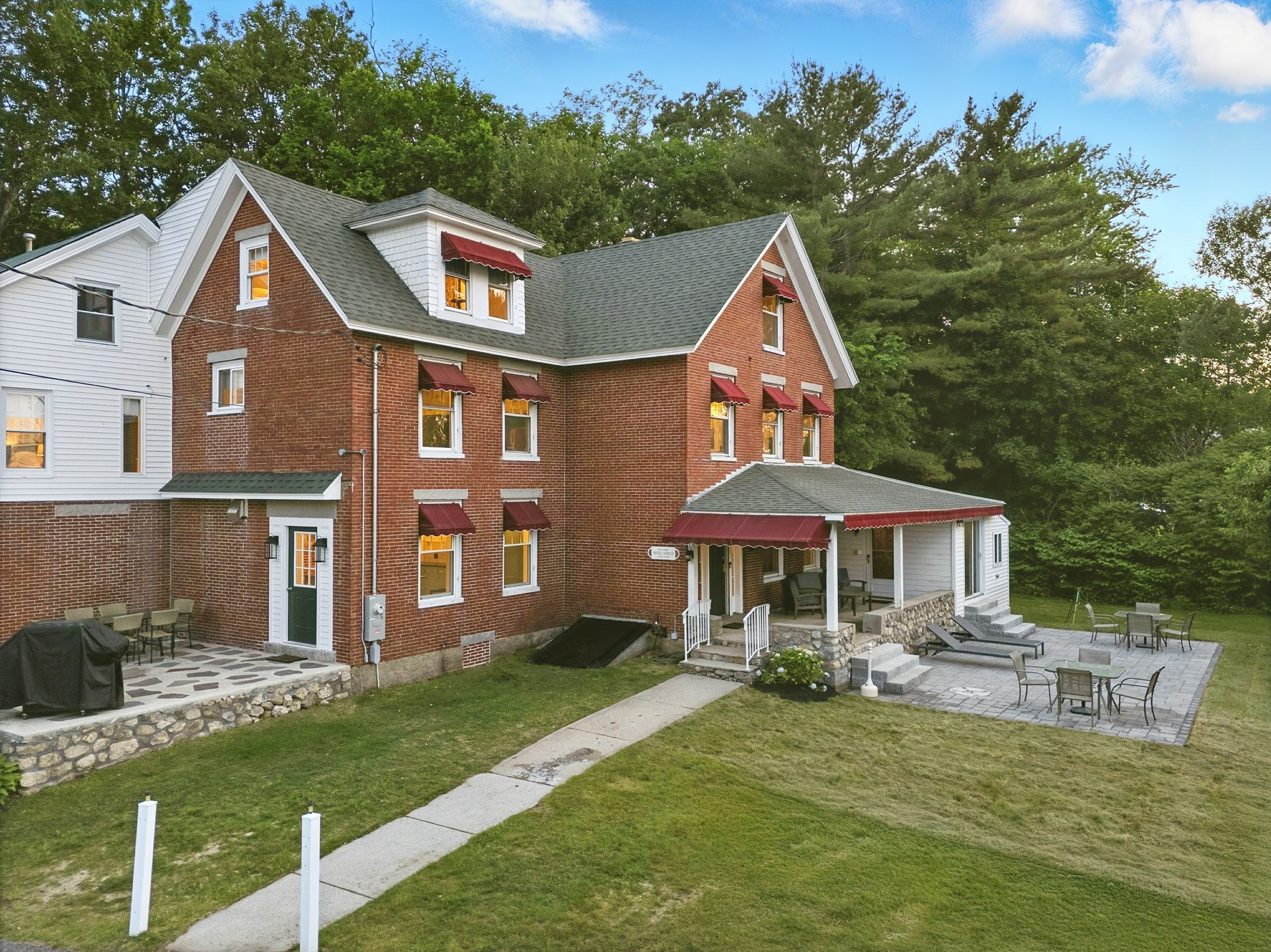 Brick multi-story house with awnings, porch, stone patio, and green lawn.