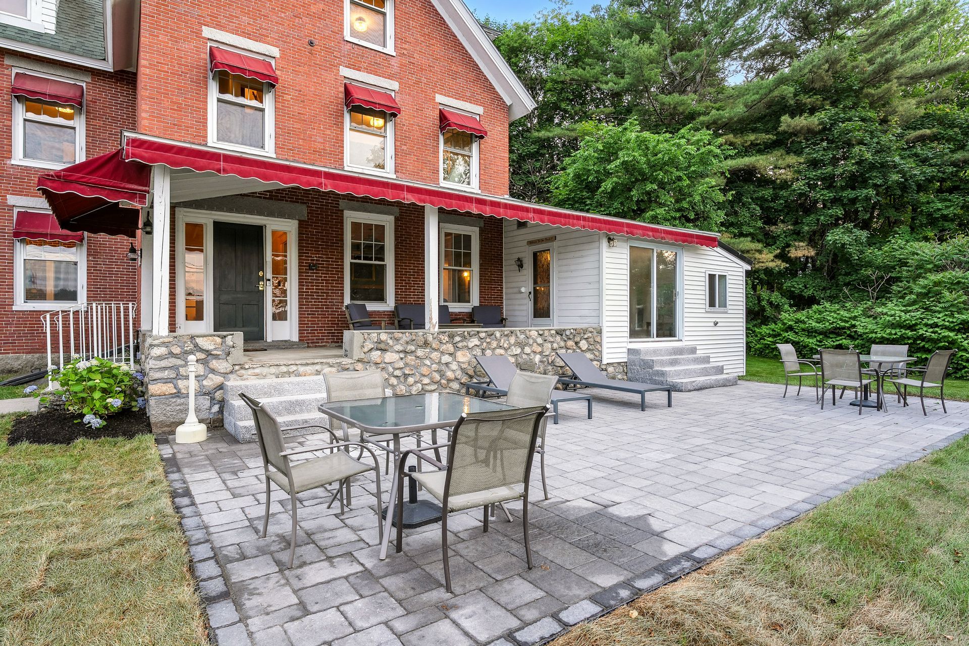 Red brick house with a front porch, patio furniture, and green lawn.