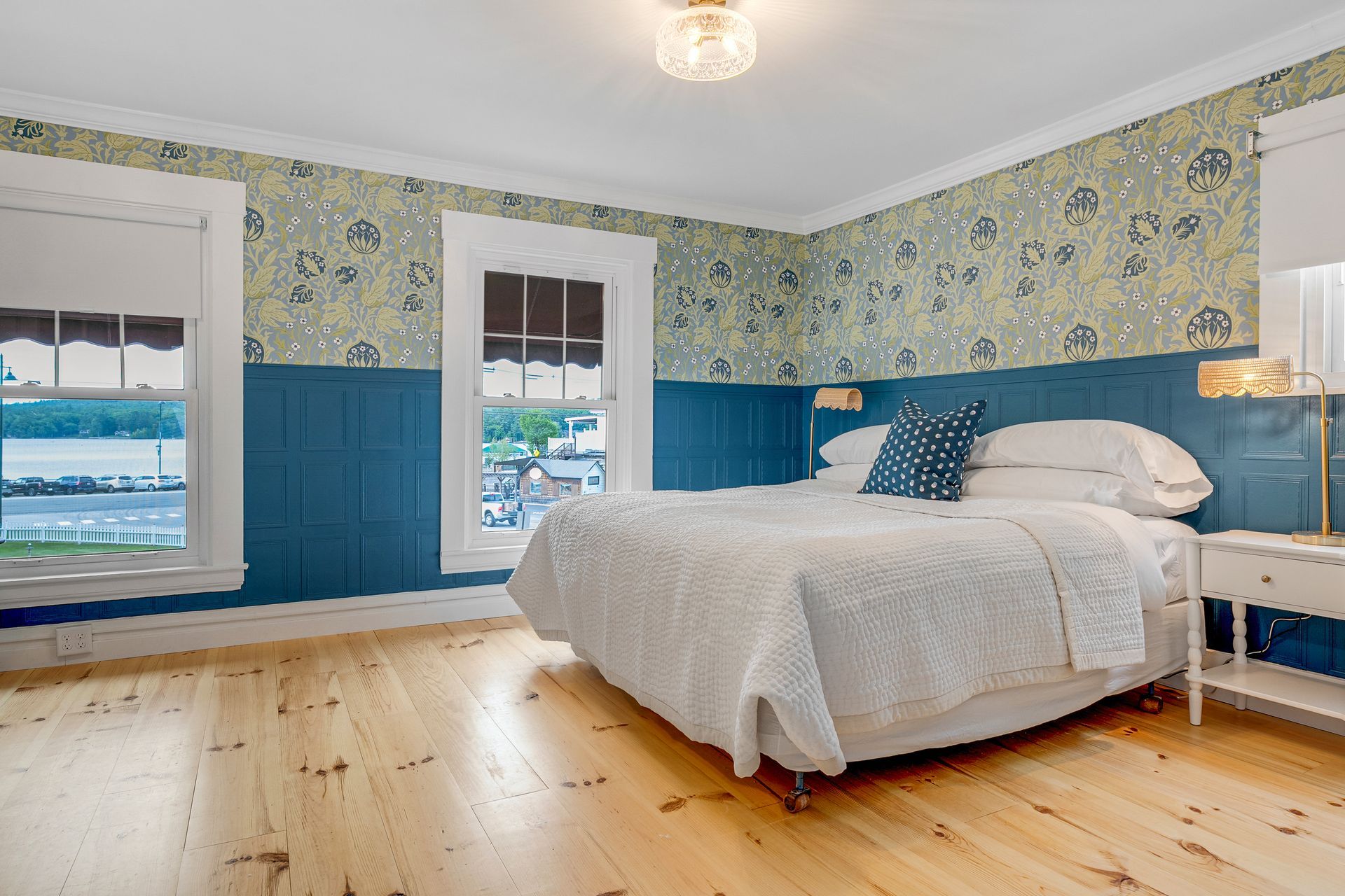 Bedroom with blue paneling, floral wallpaper, white bed, and wood floor.