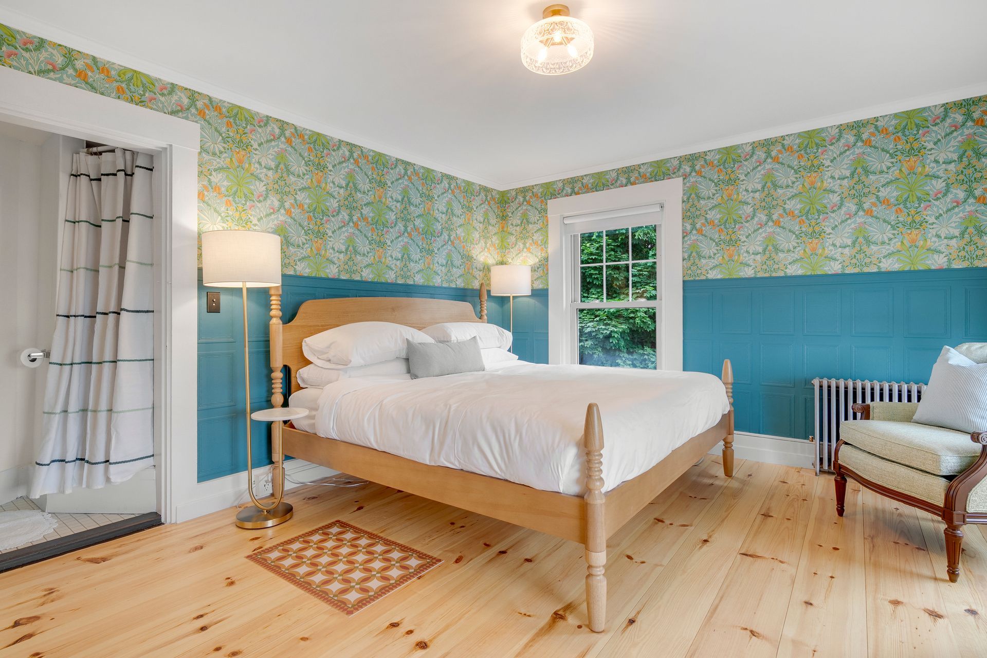 Bedroom with light wood bed, patterned wallpaper, blue paneling, and a small rug on wood floors.