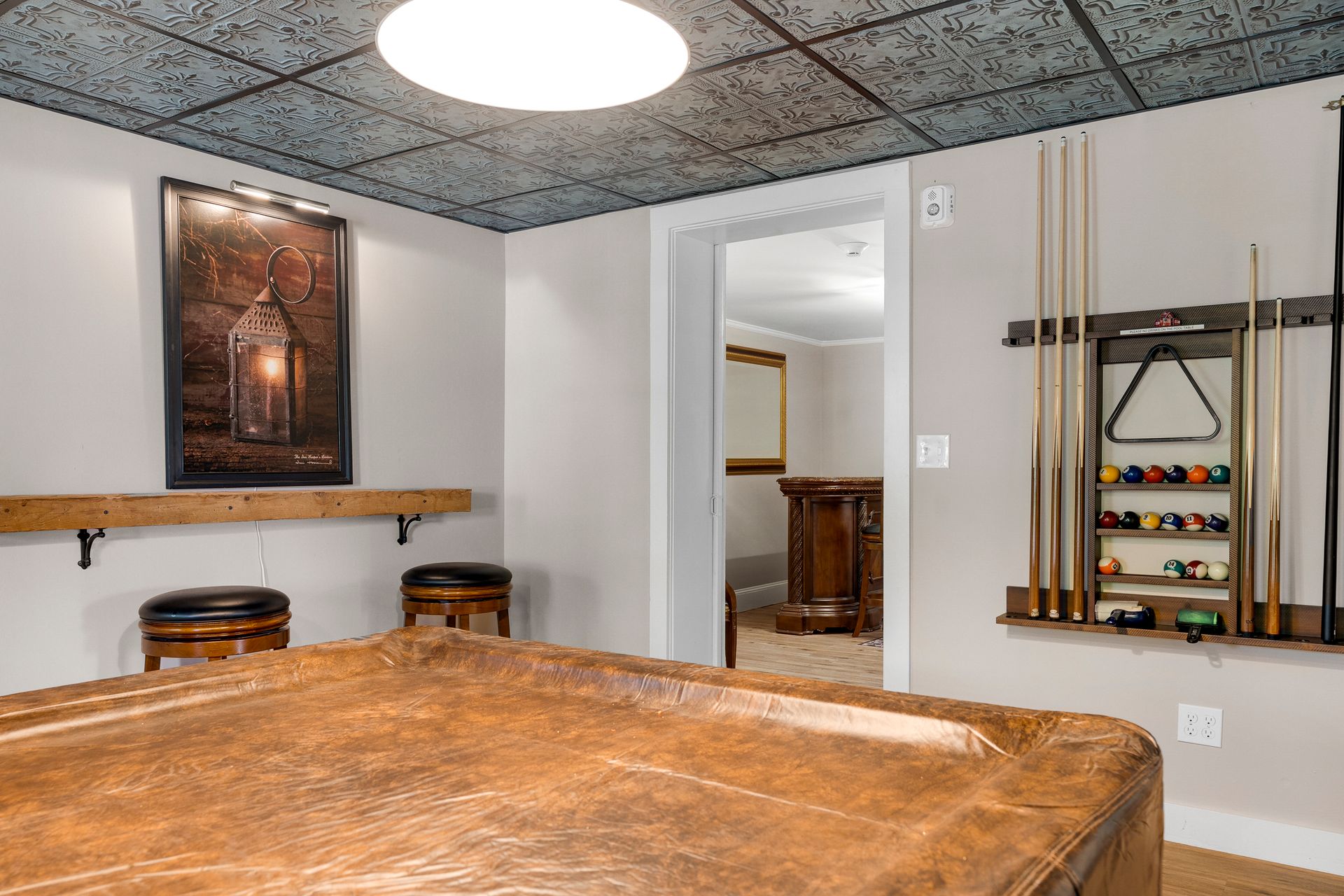 Billiard room with leather table, stools, wall rack with cues and balls, and a bar area.