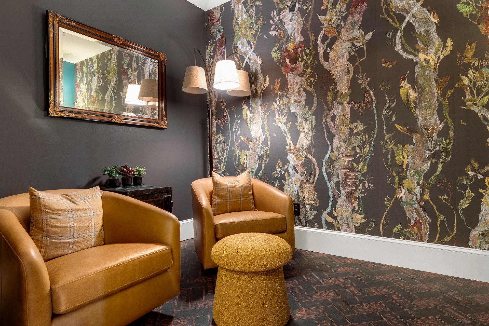 Two tan leather armchairs and footstool in room with patterned wallpaper, mirror.