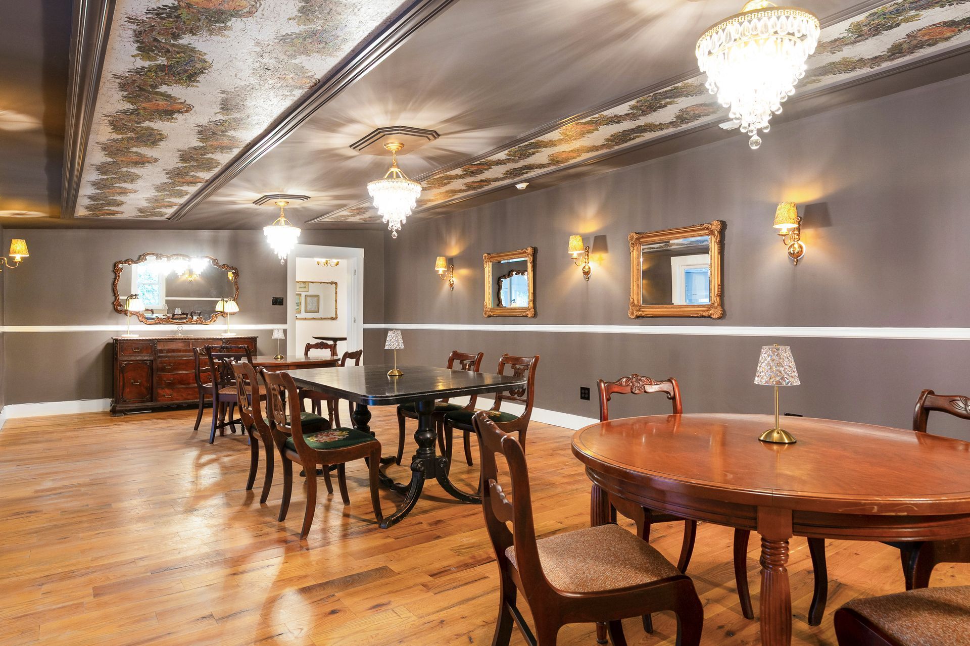 Elegant dining room with chandeliers, gold-framed mirrors, wooden tables and chairs, and a decorative ceiling.