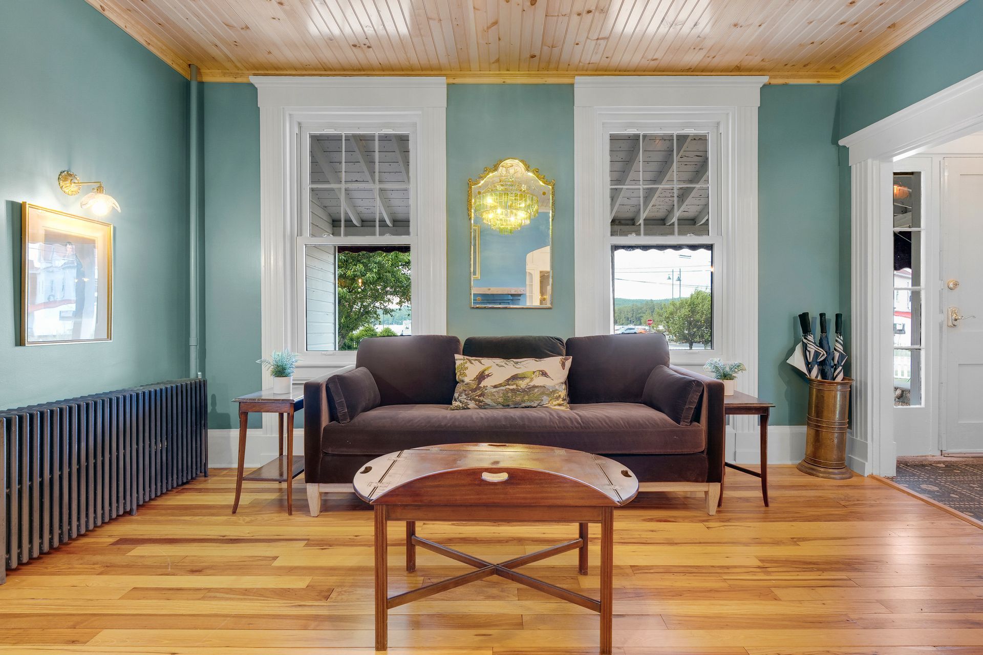 Living room with teal walls, wood floors and ceiling, brown sofa, and two windows.