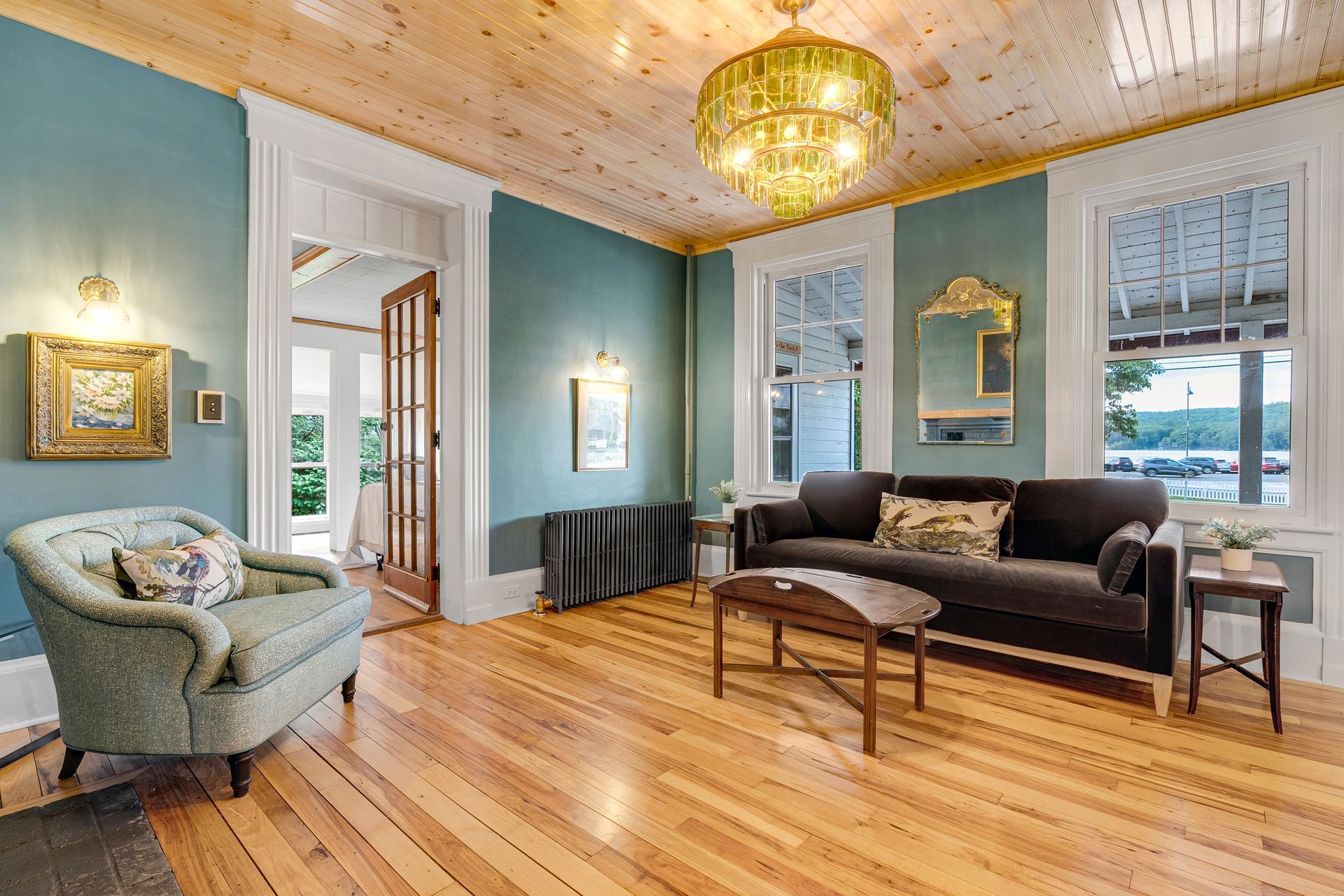 Living room with teal walls, wood floors and ceiling, sofa, armchair, and gold chandelier.