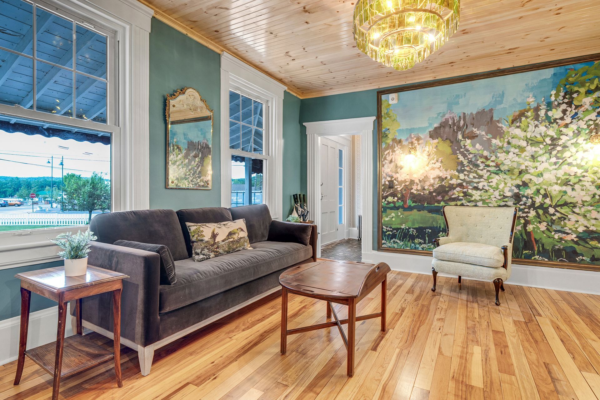Living room with teal walls, a gray sofa, wood floor, and a large mural.