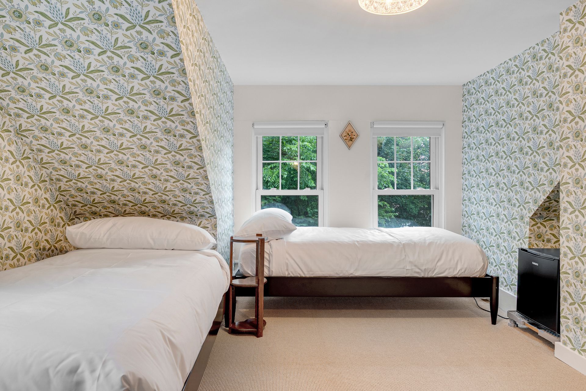 Bedroom with two beds, floral wallpaper, windows, and patterned rug.