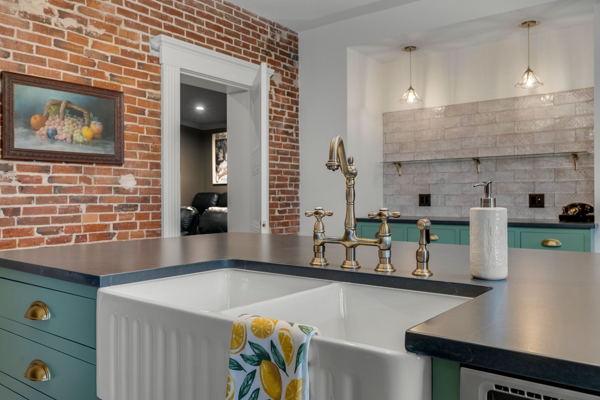 Kitchen with brick wall, farmhouse sink, gold faucet, and teal cabinets.