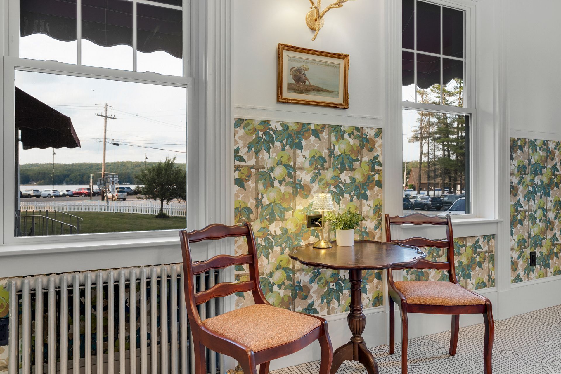 Interior with two chairs, small table, floral wallpaper, windows with lake view, and a framed art piece.