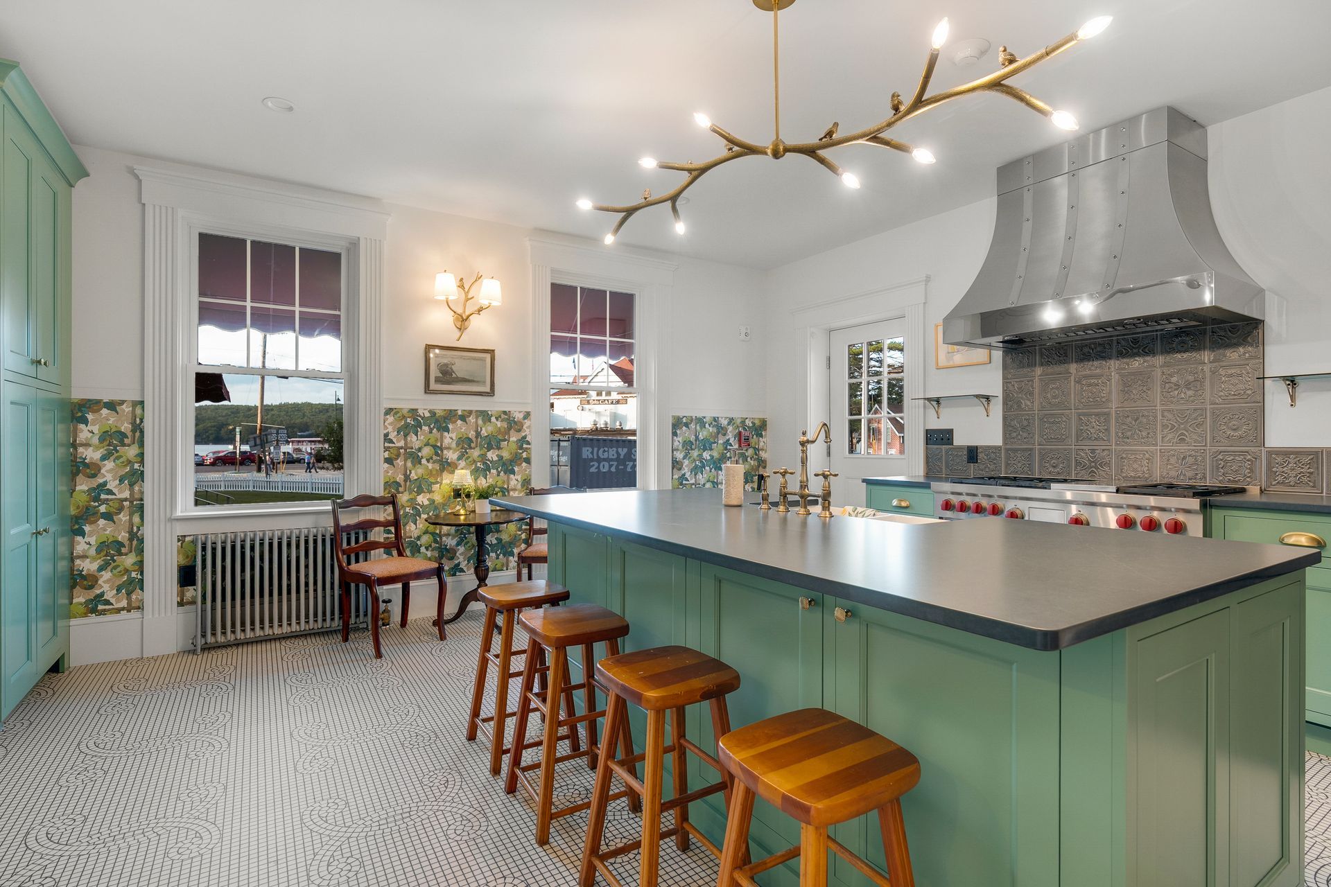 Spacious green and white kitchen with a large island, wood stools, and floral wallpaper.