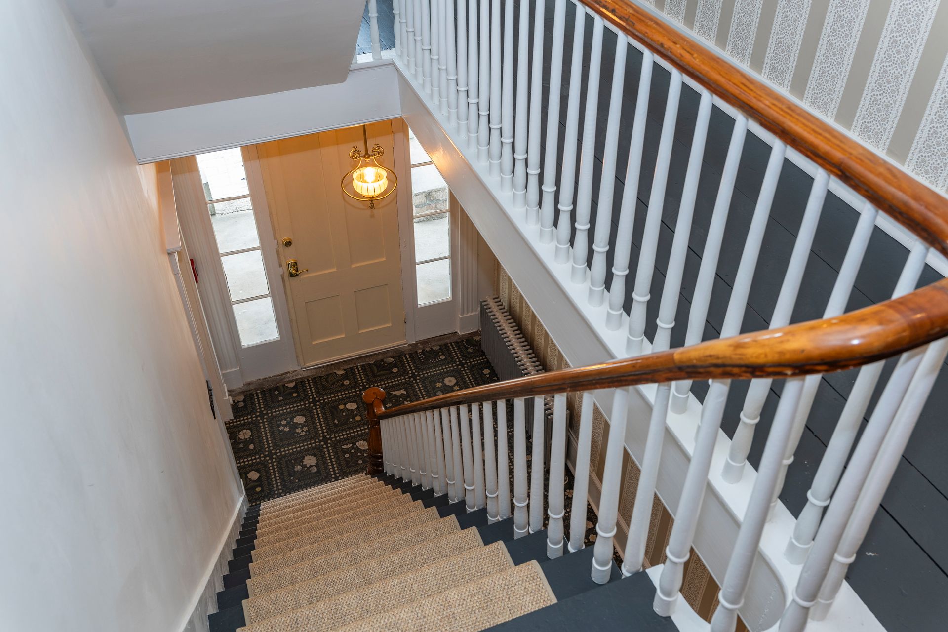 Staircase with white railing, wood handrail, leading down to a front door with sidelights.