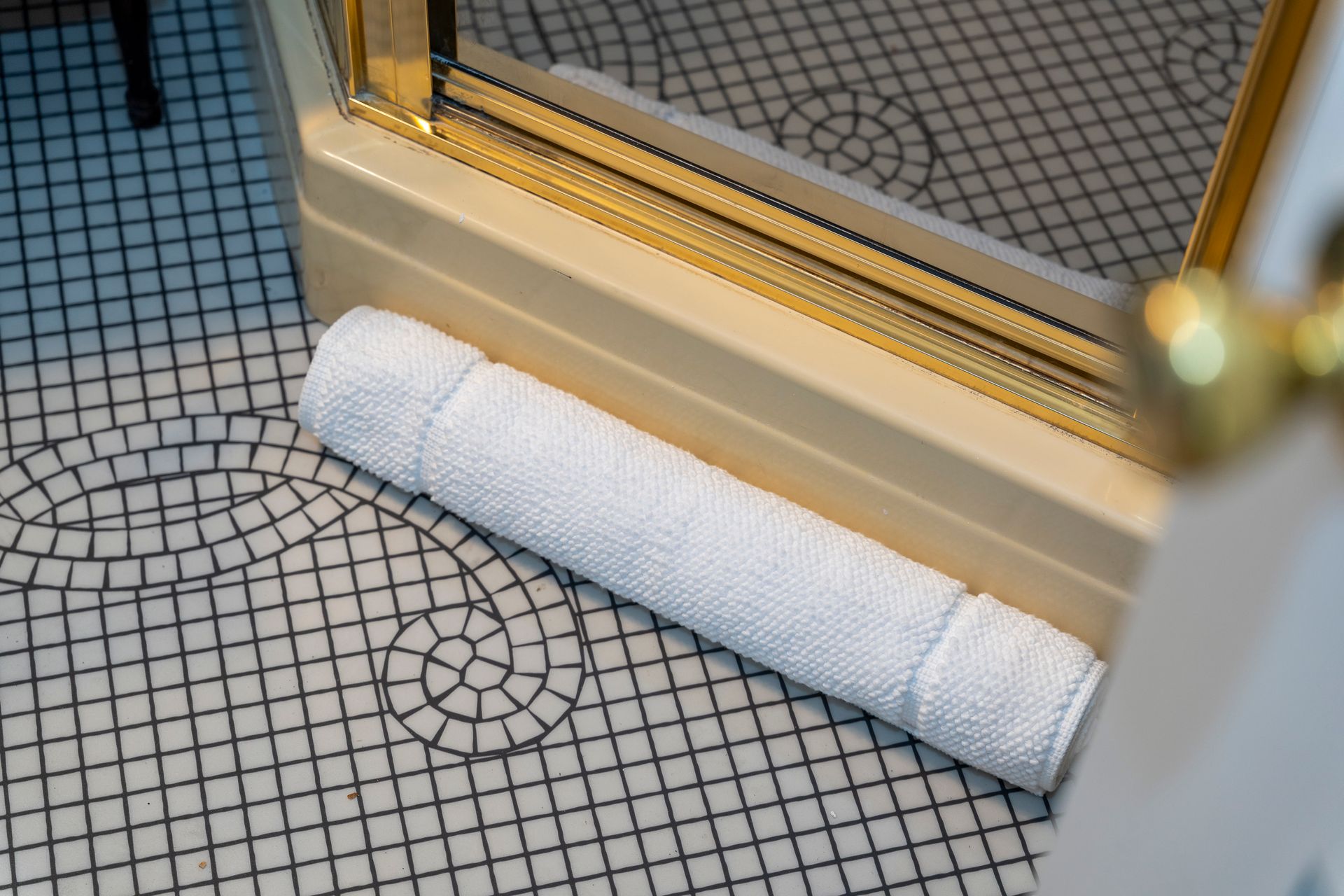 White rolled towel on patterned floor near a cream-colored mirrored vanity.