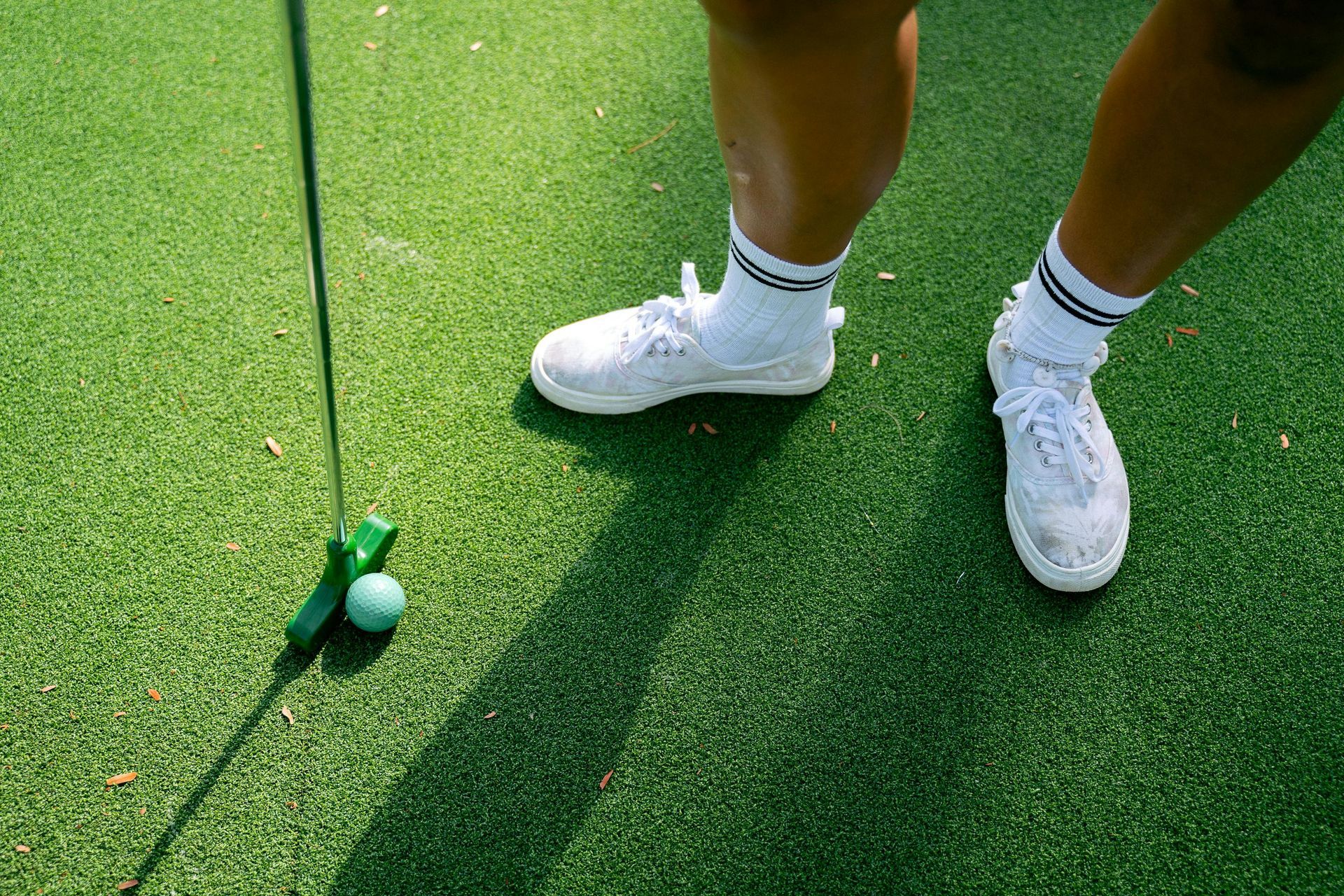 Person putting a golf ball on a green, wearing white sneakers and socks.