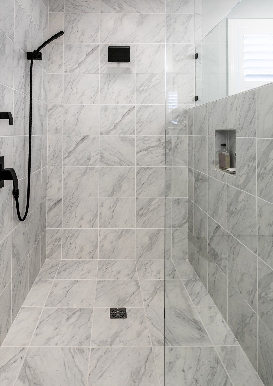 a modern shower made with white marble and glass doors.