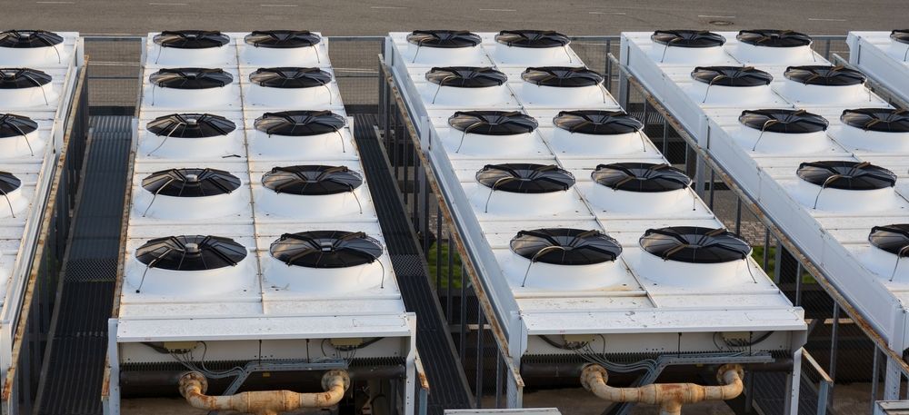 Rows of industrial cooling units on a rooftop, white with black fan tops.