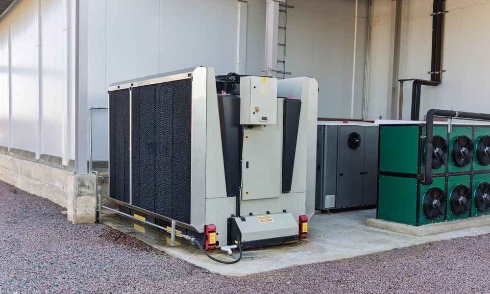 Exterior view of industrial cooling equipment against a white building. Gray and green machinery sits on a concrete pad.