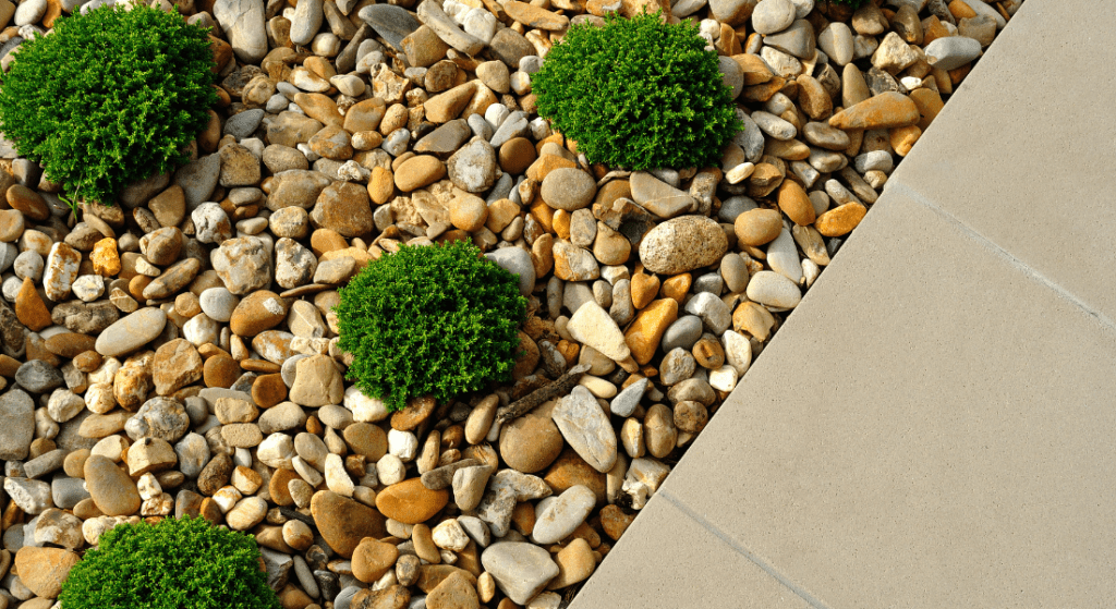 A pile of rocks and plants next to a sidewalk.