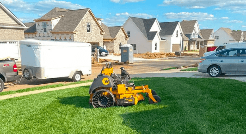 A lawn mower is cutting a lush green lawn.