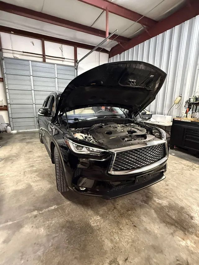 A black Infiniti SUV with its hood open in a professional garage with a concrete floor and a metal roll-up door. | Bucks Auto Garage & Tire