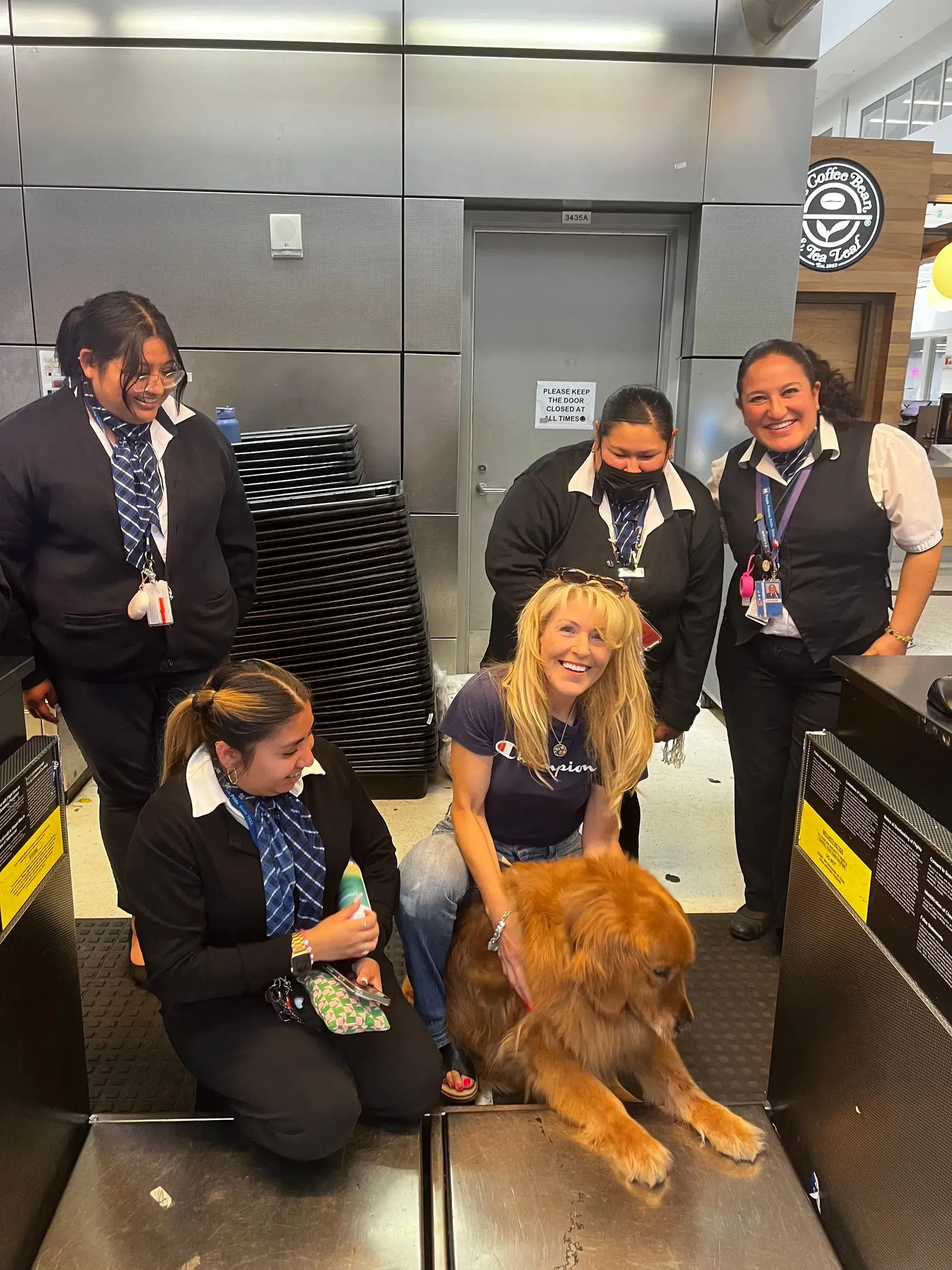 Five people in navy uniforms pose with a golden retriever in a metallic room.