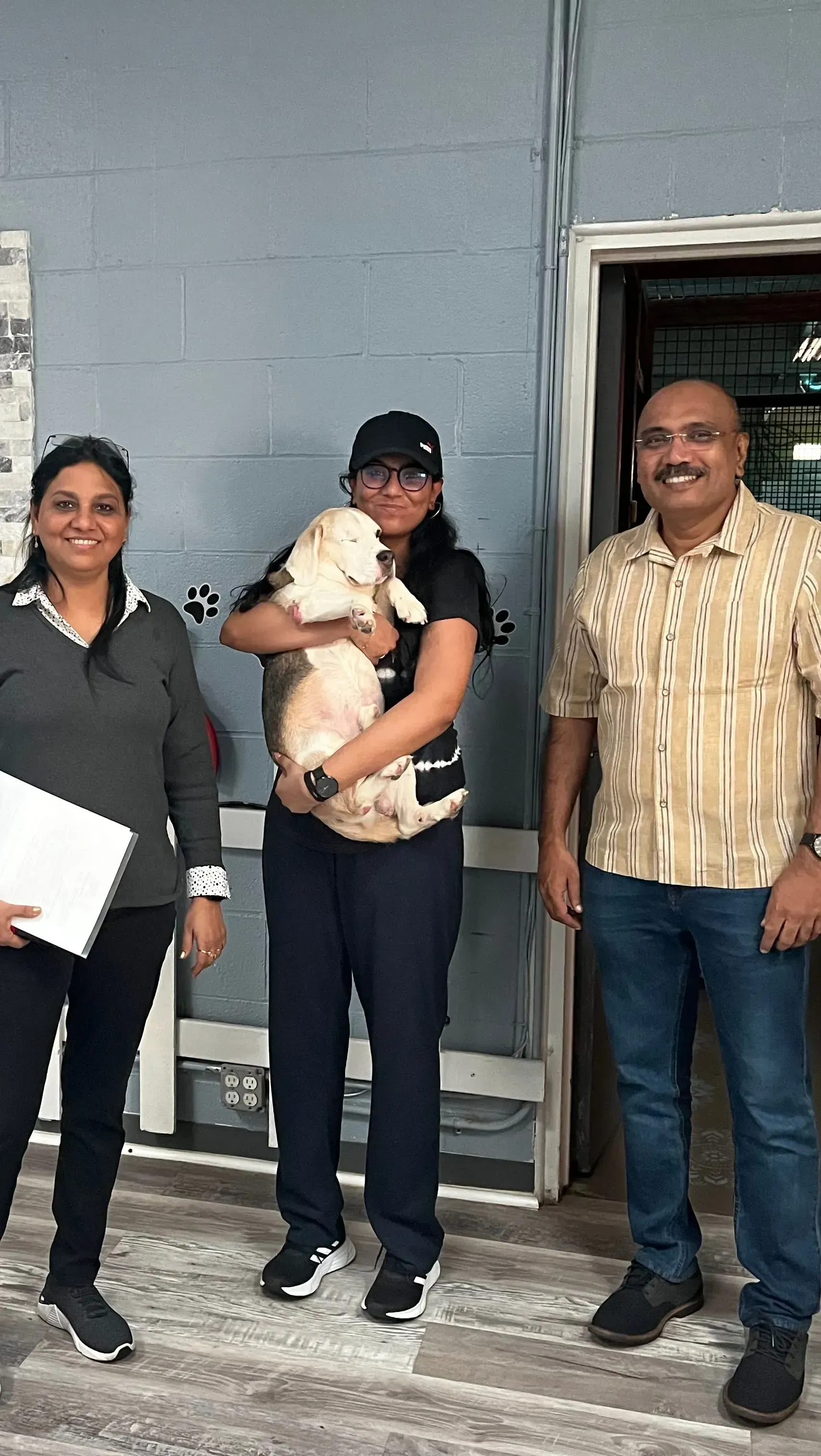 Three people standing outside a building; the center person holds a small dog.