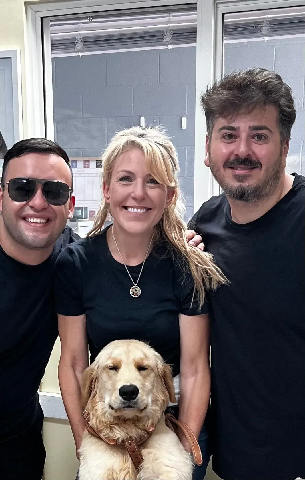 Three people smiling with a golden dog in front of a window.