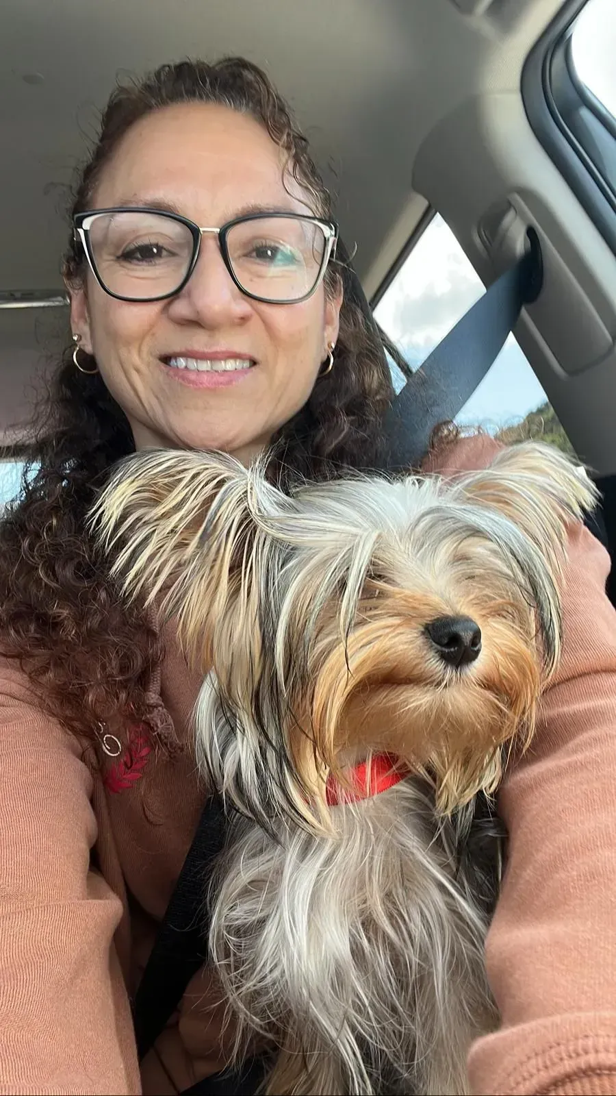 Woman in a car smiling with a small Yorkshire terrier on her lap