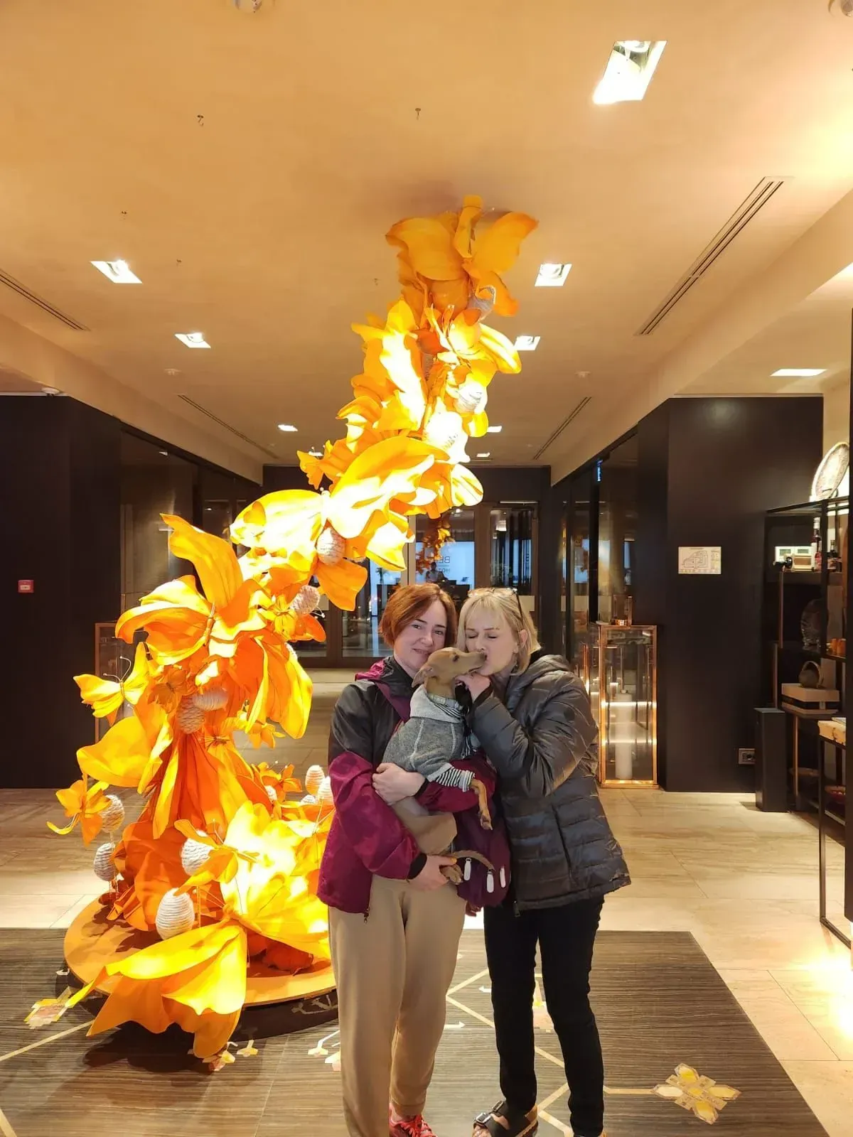 Two people posing indoors beside a tall orange leaf sculpture in a lobby.