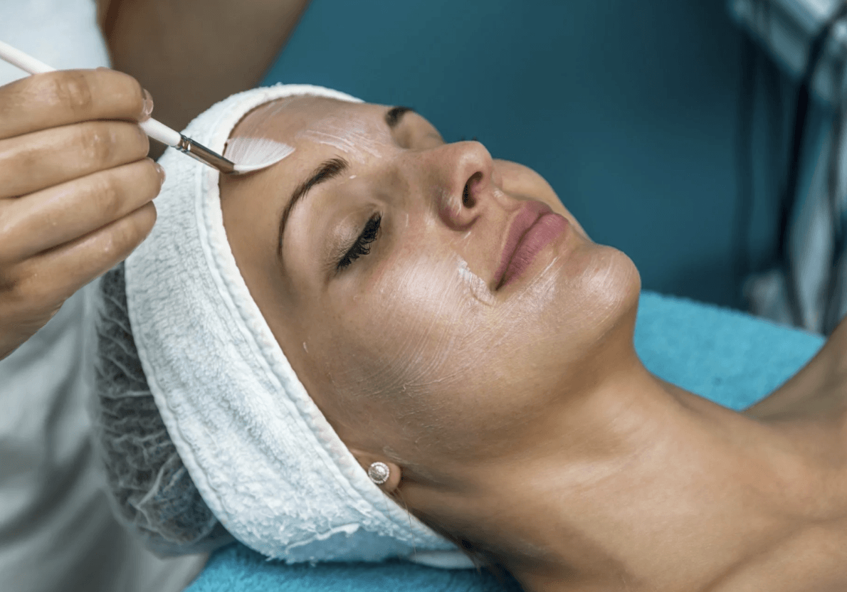 Woman receiving a chemical peel treatment with a facial brush while lying on a spa bed