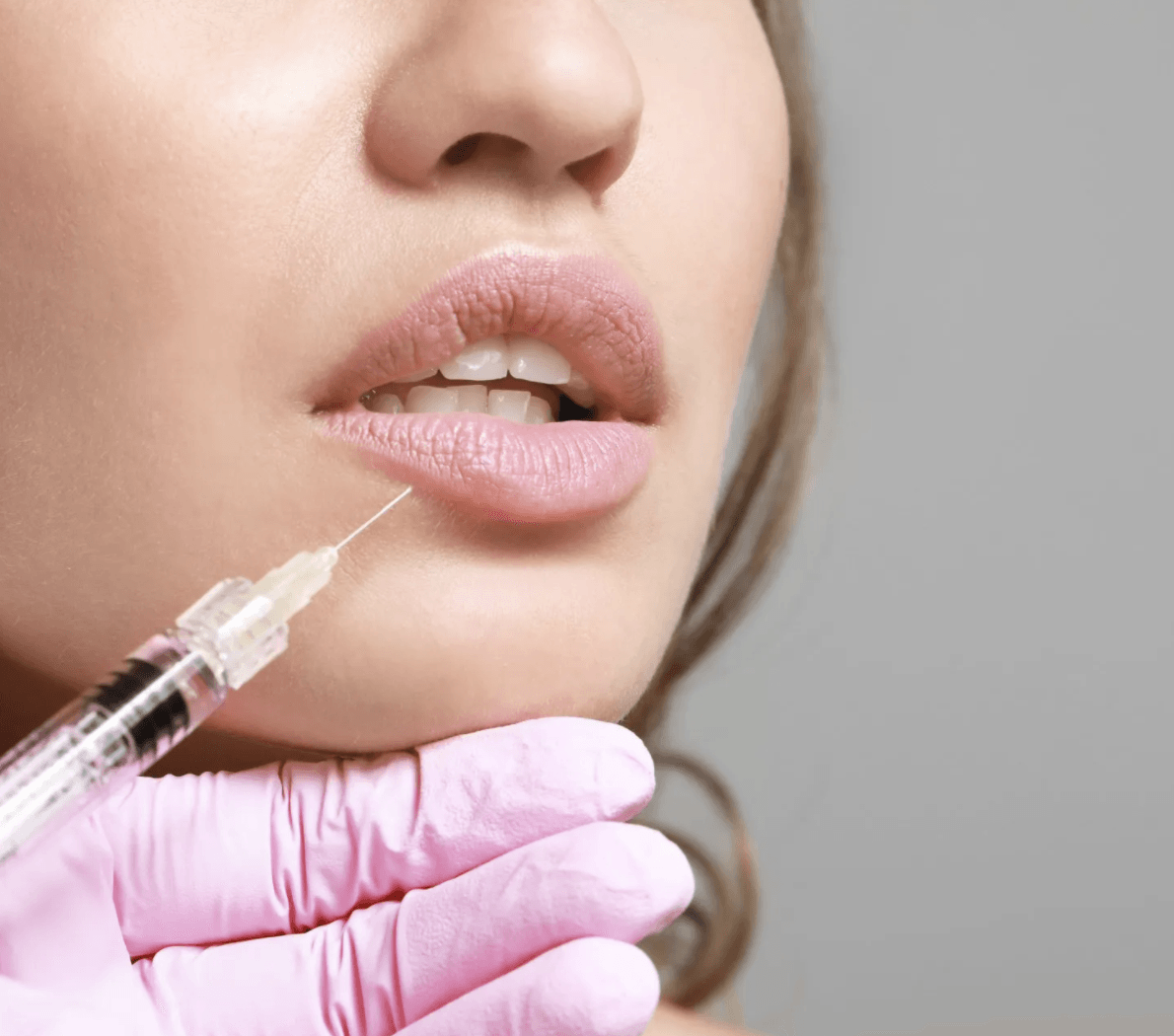 Close-up of woman receiving lip filler injection by professional wearing pink gloves