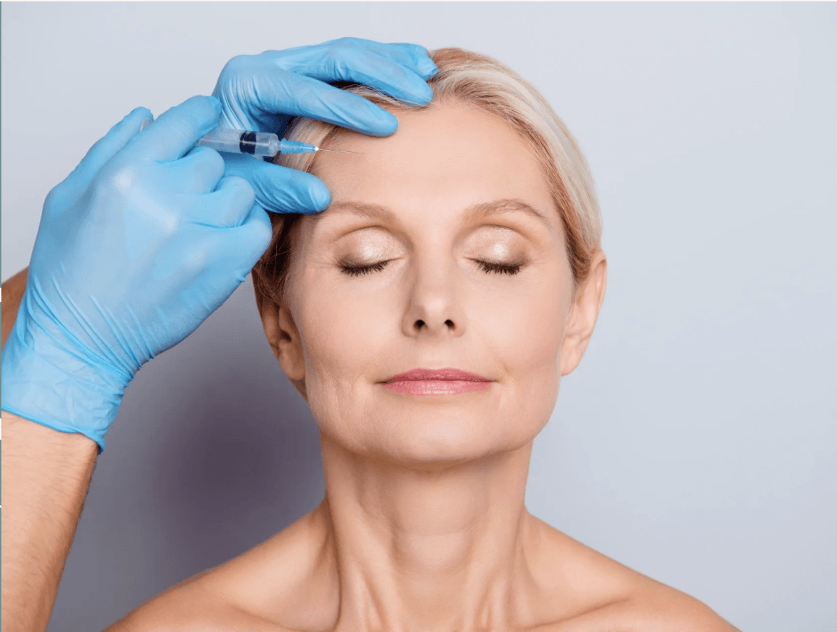 Middle-aged woman receiving wrinkle relaxer injection in forehead with gloved medical professional