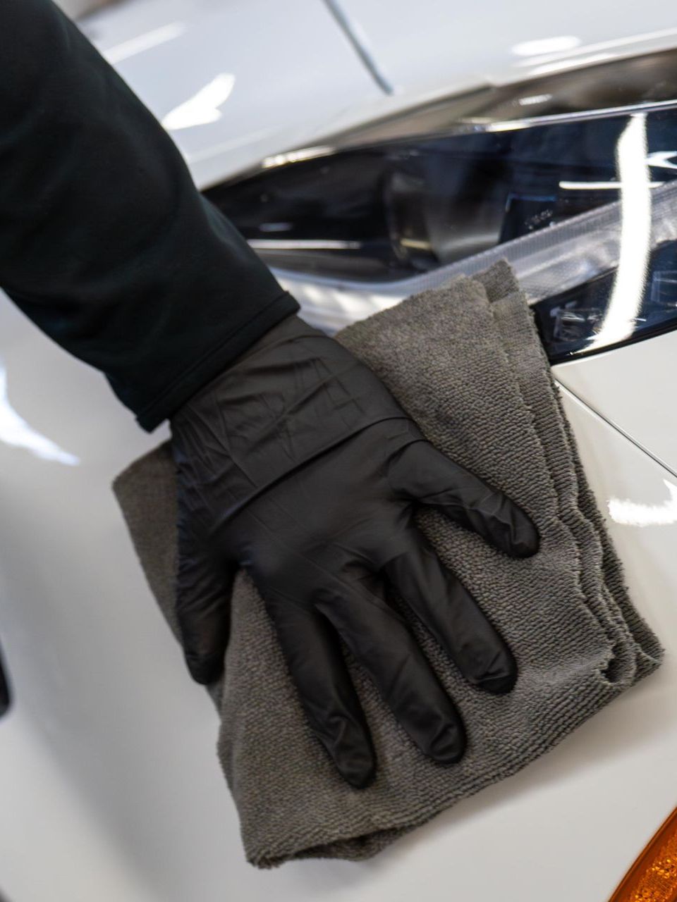 A person wearing black gloves is cleaning a car with a towel