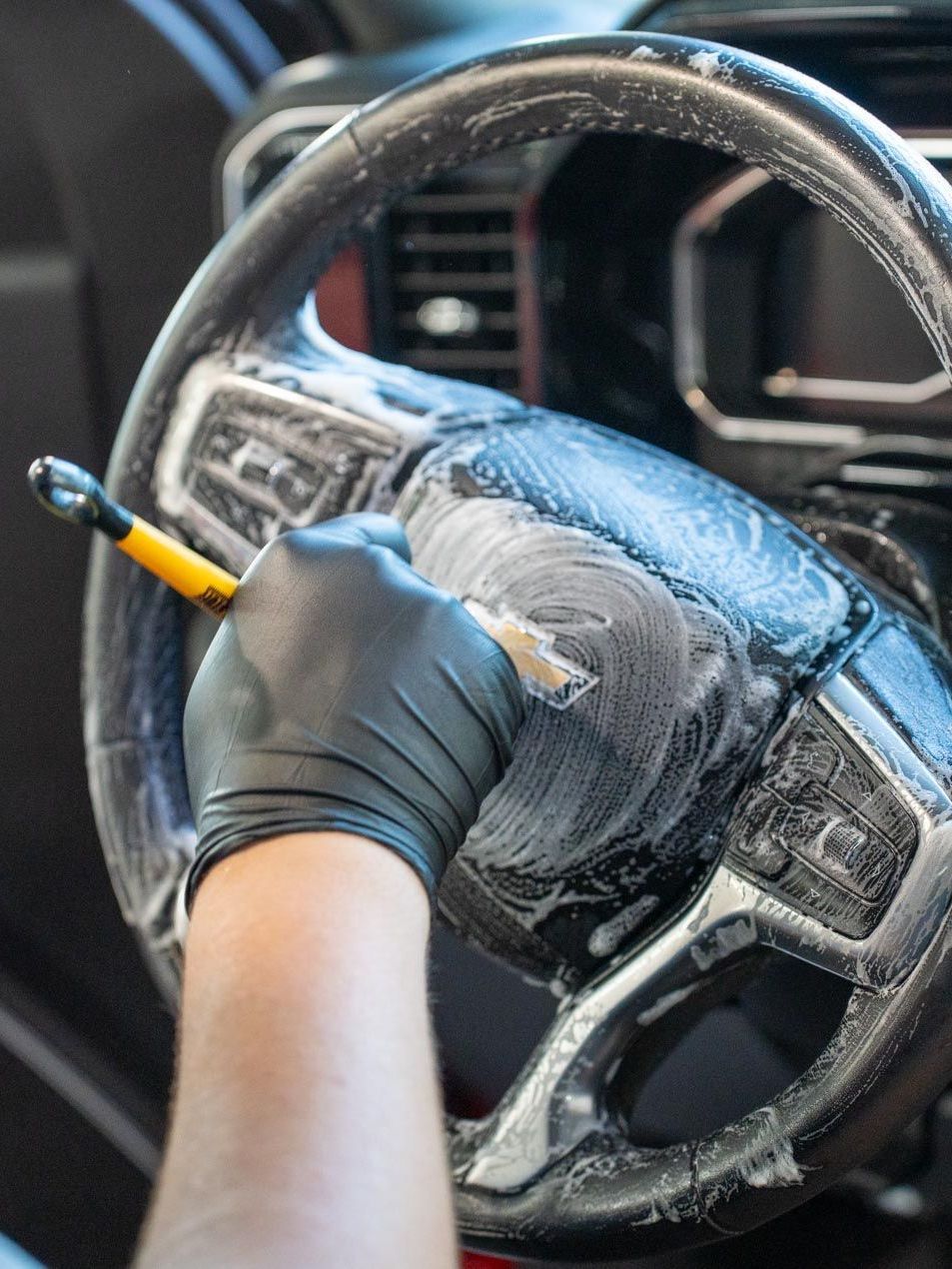A person is cleaning a car steering wheel with a brush.