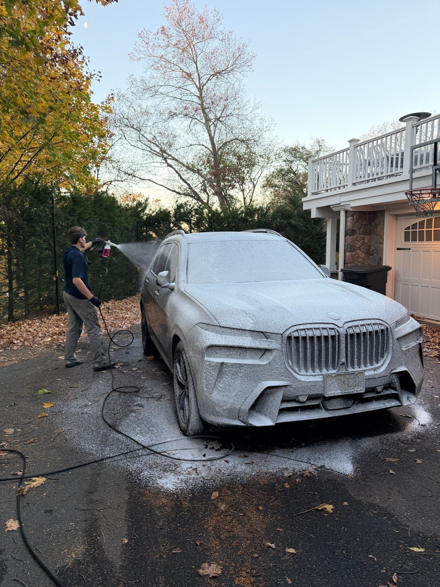 A man is washing a car with foam in front of a house.