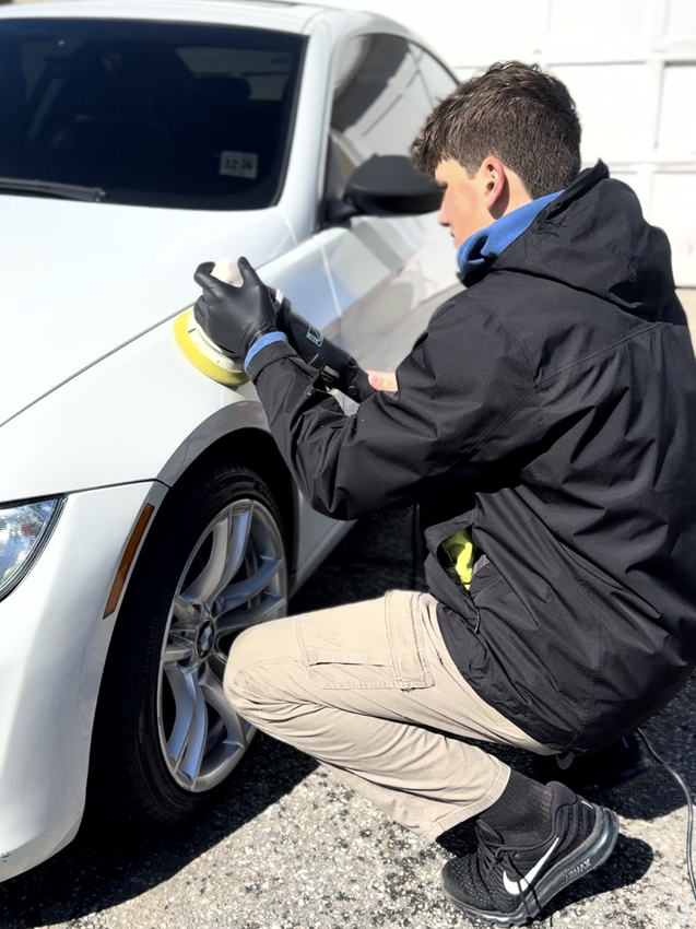 A man is cleaning the wheel of a black car with a sponge.