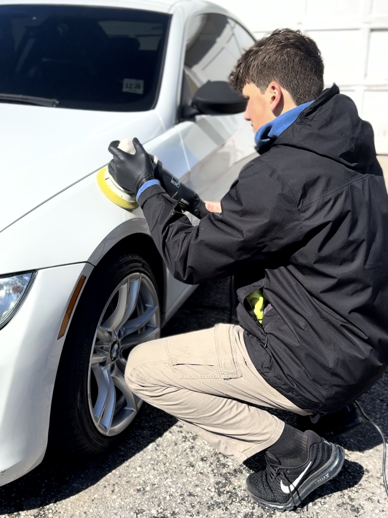 A person wearing black gloves is polishing a black car