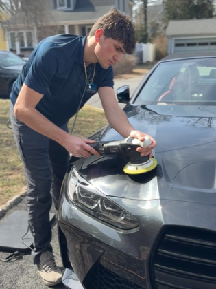 A person is using a blue squeegee to remove plastic from the hood of a car