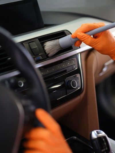 A person wearing orange gloves is cleaning the dashboard of a car with a brush.