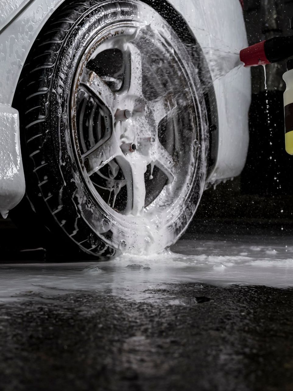 A person is washing a car wheel with foam.