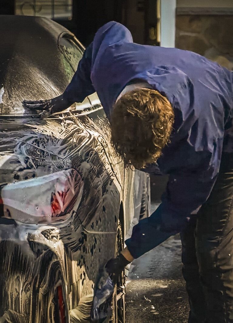 A man is cleaning the wheel of a black car with a sponge.