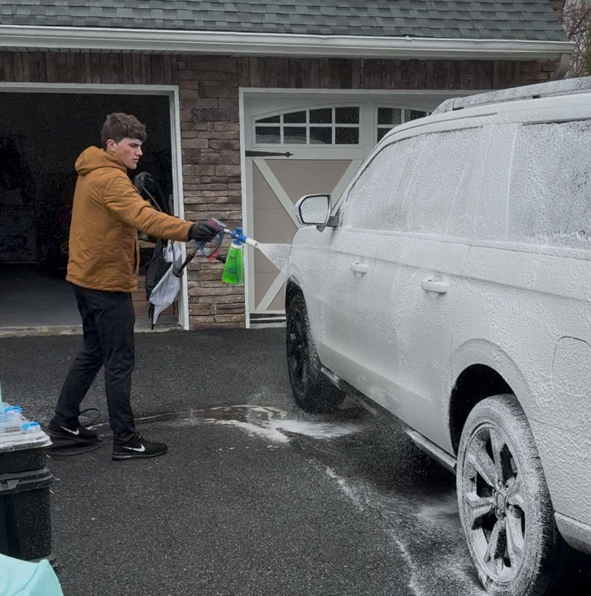 A man is cleaning the wheel of a black car with a sponge.