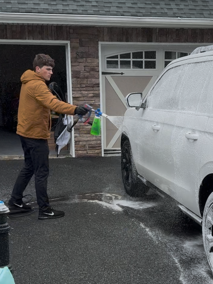 A man is washing a white suv in front of a garage.