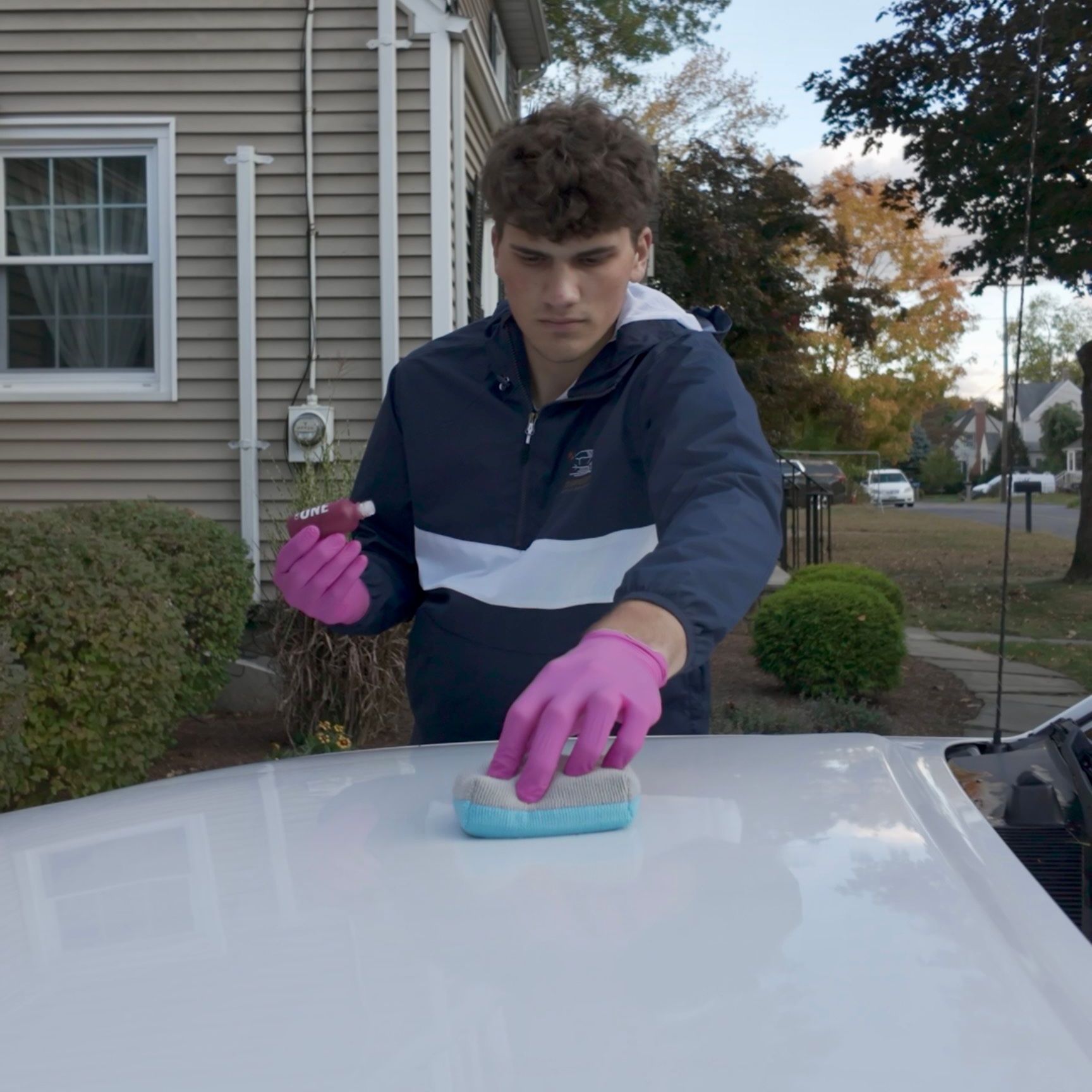 A man wearing pink gloves is cleaning the hood of a car