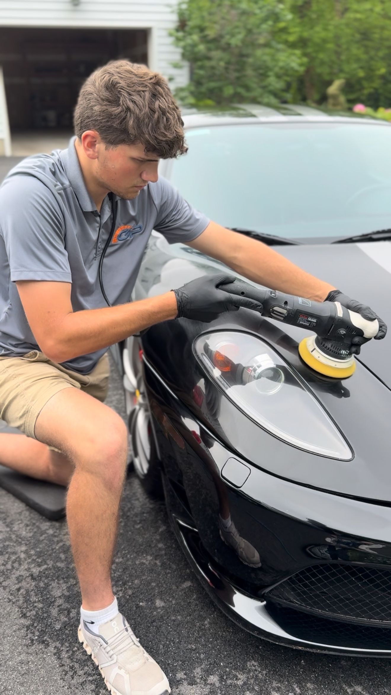 A young man is kneeling down in front of a blue car.