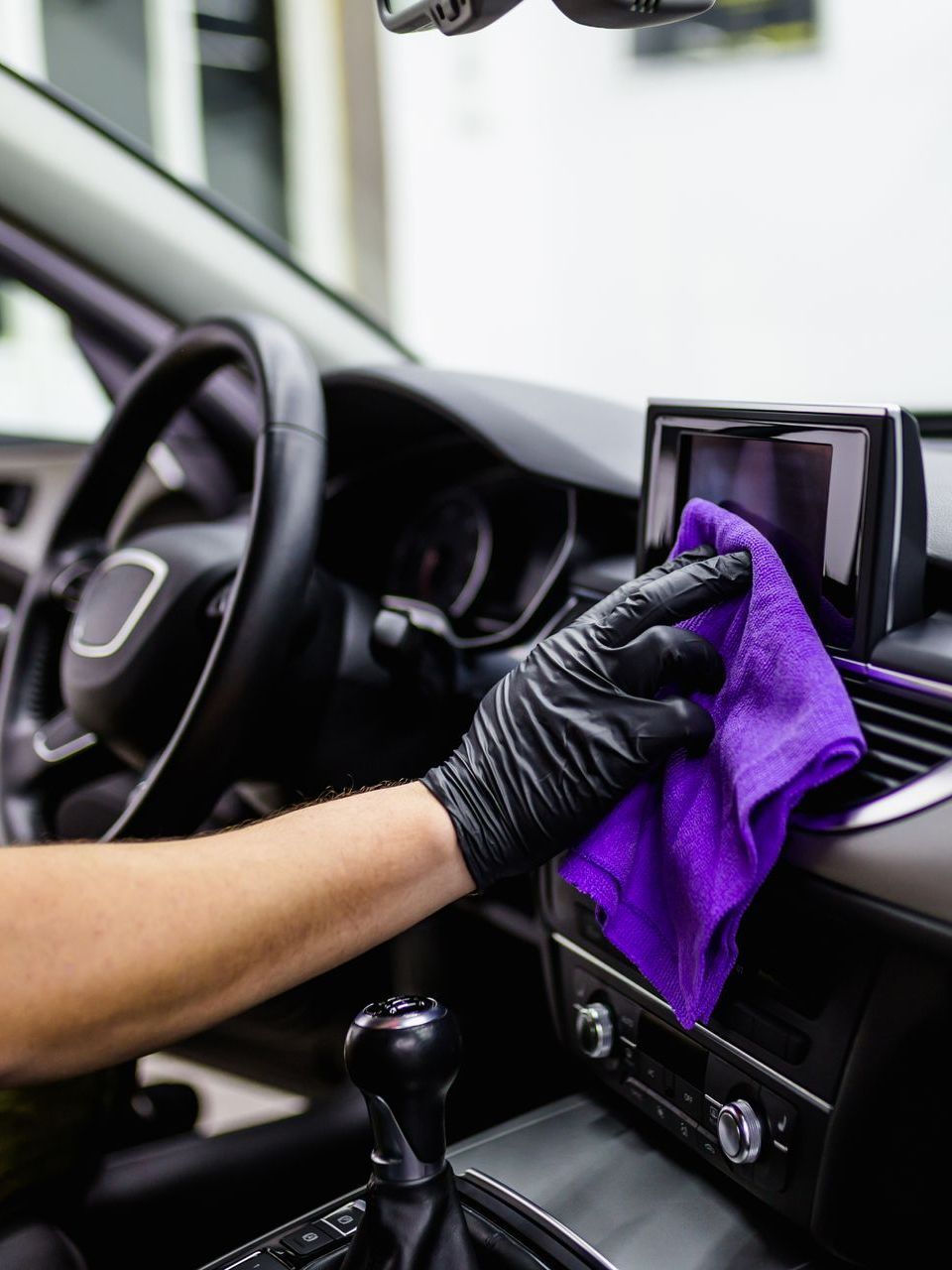 A person is cleaning the dashboard of a car with a purple cloth.