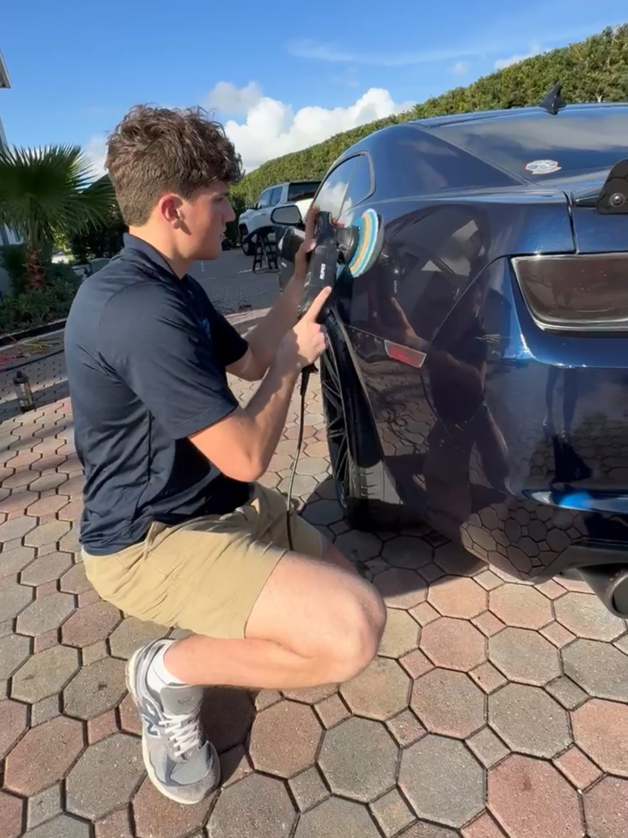 A person is polishing a yellow sports car with a machine.