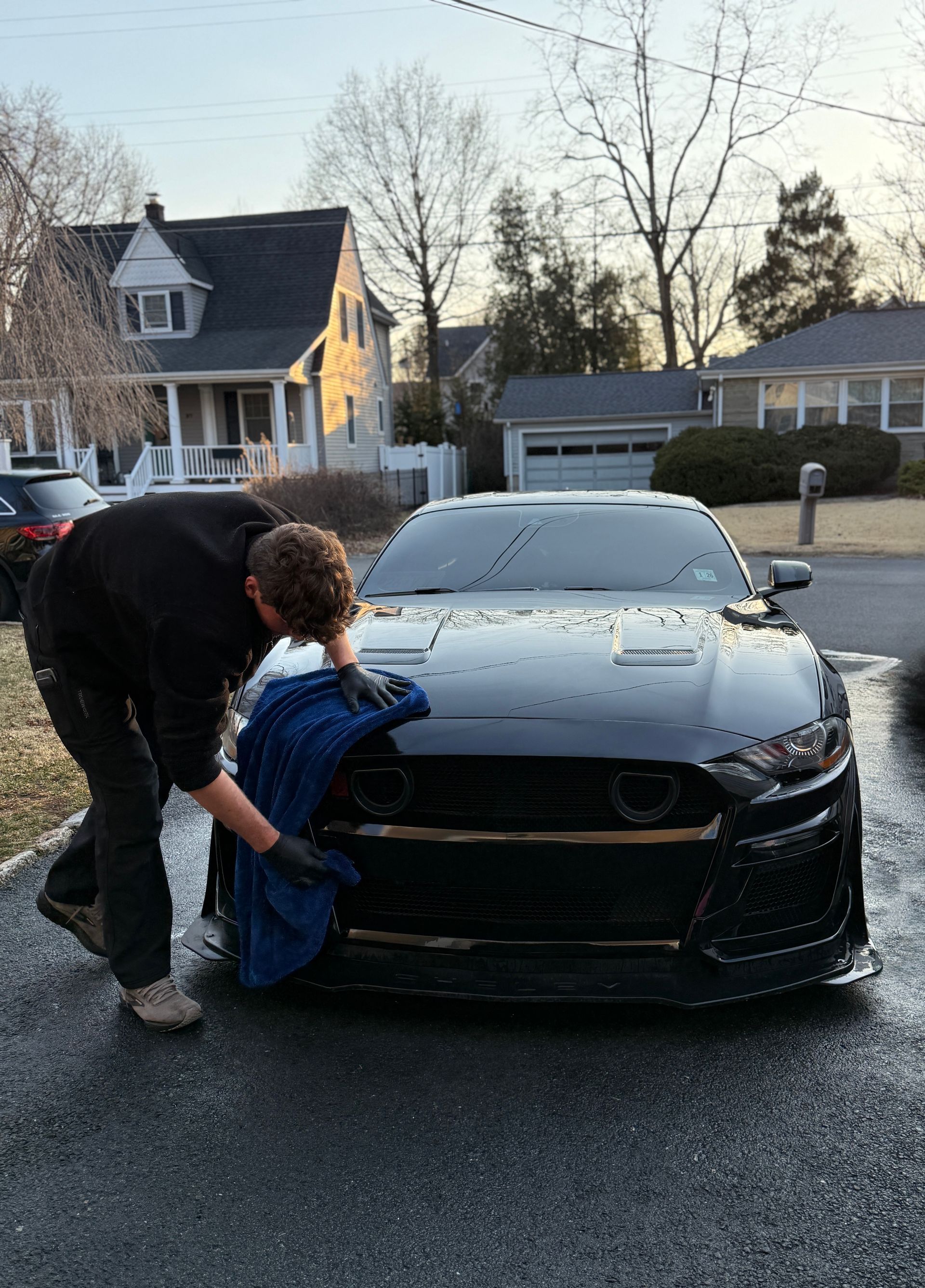 A man is washing a car with a towel in front of a house.
