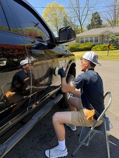 A man is sitting on a chair polishing a car.