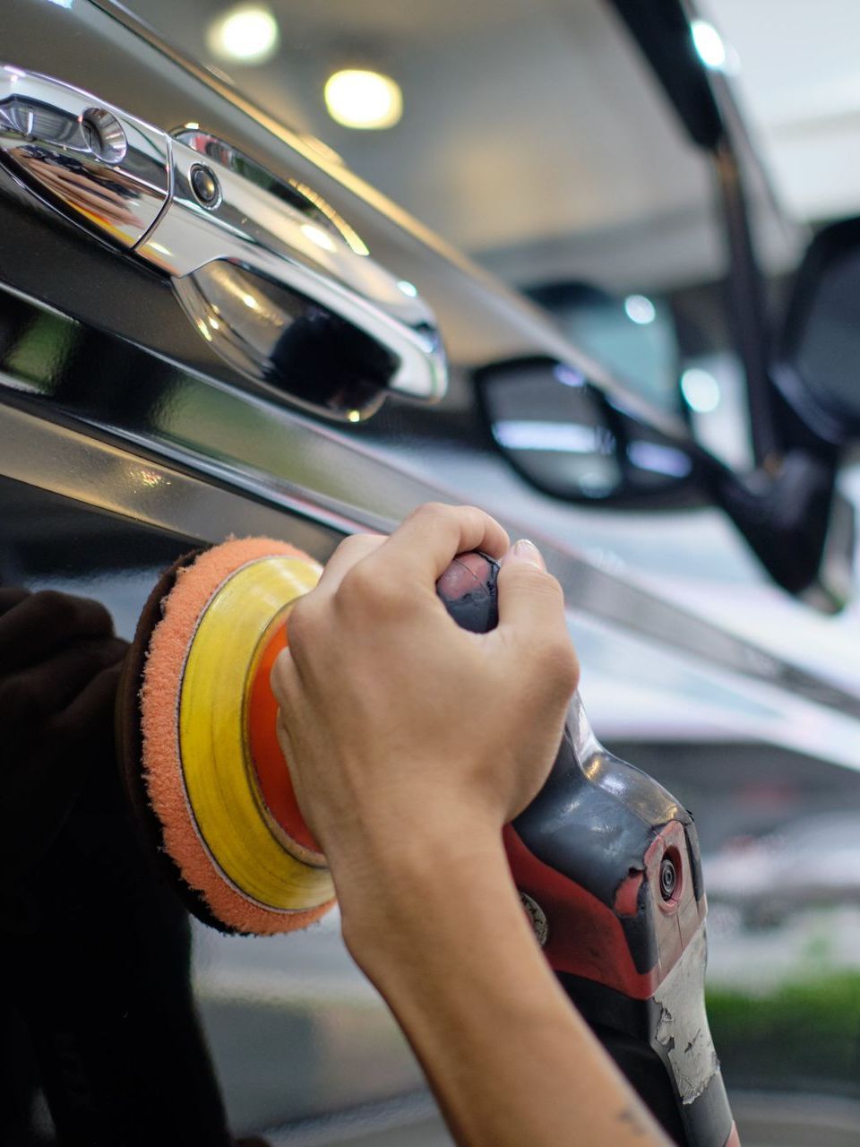 A person wearing black gloves is polishing the hood of a red car.